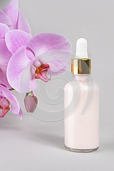 Pink anti-aging collagen, facial serum in transparent glass bottle with gold pipette and natural orchid flower on grey background