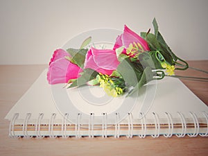 Pink artificial roses flower of bouquet on book with spiral