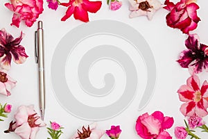 Pink azalea flowers with silver pencil and empty paper sheet, top view, space for text, flat lay