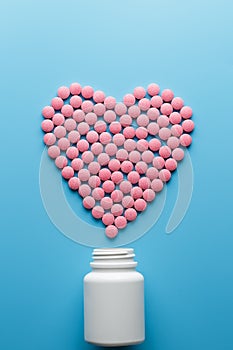 Pink B12 pills in the shape of a heart on a blue background, poured out of a white can