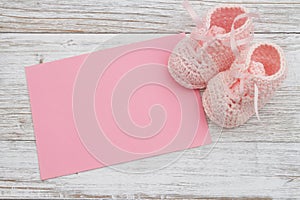 Pink baby booties with pink greeting card on weathered wood