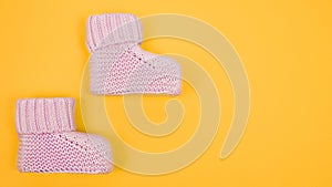 Pink baby booties on yellow background. Copy space, 16x9 banner.
