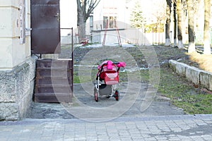 Pink baby carriage stand outdoors near stairs to the house in sunny day without parents. Irresponsibility young mother