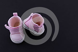 Pink baby shoes on a black background. The concept of first steps, birthday, expectation, pregnancy, motherhood, motherhood,