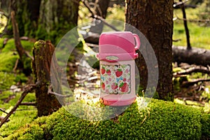 Pink baby thermos for drinks. Thermos in the forest on moss