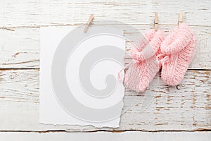 Pink baby's booties. Small girls sock and blank card on white wooden background