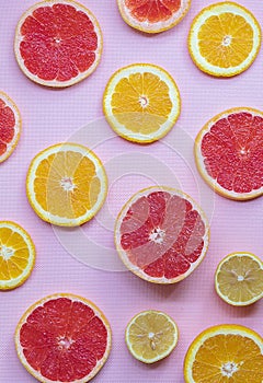 On the pink background lie juicy and ripe slices of orange, lemon and grapefruit