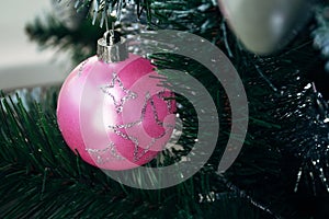 Pink ball on artificial Christmas tree. Selective focus. Holiday card with decorations for the New Year`s Eve