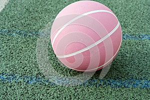 Pink basketball ball on the ground. Close-up ball on the red court. Basketball on the street or indoor court. Sports gear