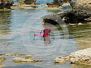 a pink beach chair sits in the water in the middle of a rocky lagoon. Paralimni. Ayia Napa. Cyprus