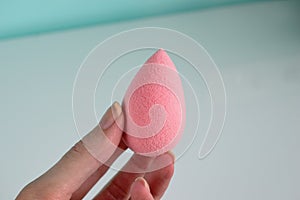 Pink beauty tear-shaped blender, clean sponge isolated on white background. Cosmetic tool for makeup in hand.