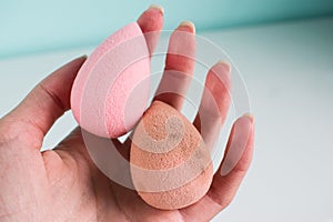 Pink beauty tear-shaped blender, dirty and clean sponges  on white background. Cosmetic tool for makeup in hand.