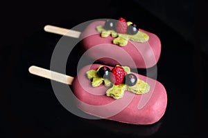 Pink berries and pistachio gelato ice cream on stick with raspberries, black currants and pistachio sponge