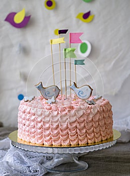 Pink birthday cake with birds topper and flags against a white background, space for text. Romantic love concept