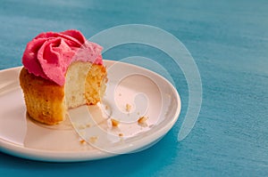 Pink bitten cupcake on a plate isolated on blue background. Delicious cake. Top view