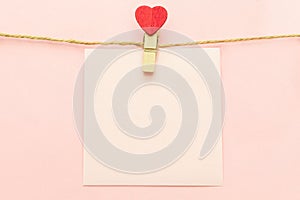 Pink blank paper sheet on a clothes line and clothespegs with red heart on a pink background. Valentines day concept