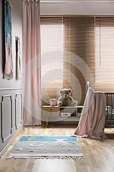 Pink blanket on bed and rug in bright baby`s room interior with