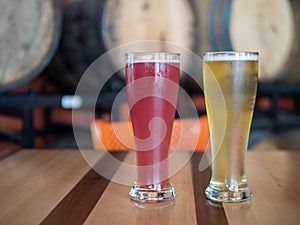 Pink and blond tall cold glasses of beer on table in front of barrels in brewery