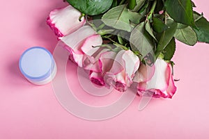 Pink blooming roses and face cream on pastel pink background. Romantic skincare floral frame. Copy space