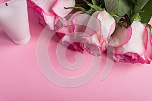 Pink blooming roses and face cream on pastel pink background. Romantic skincare floral frame. Copy space