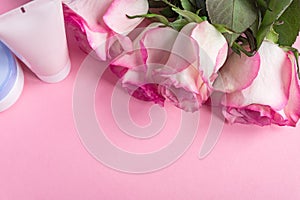 Pink blooming roses and face cream on pastel pink background. Romantic skincare floral frame. Copy space