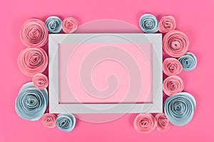 Pink and blue flower flat lay with empty picture frame surrounded by romantic paper craft roses on pastel pink background