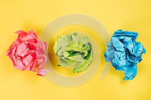 Pink, blue and green crumpled paper balls on bright yellow background