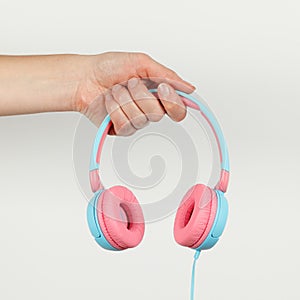 Pink-blue headphones in hand on a white background. Music services, podcasts, and streaming audio