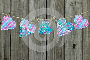 Pink and blue hearts hanging on clothesline by shabby wood fence