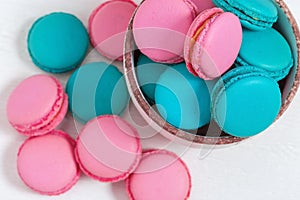 Pink and blue macaroons in bowl on wooden white background with copy space.