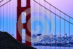 Pink blue sky and the full moon is visible through the north tower of the Golden Gate Bridge in San Francisco