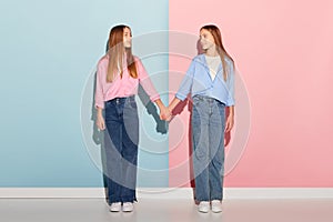 Pink and blue. Stylish couple of teen girls in trendy warm clothes looking at each other  over colorful