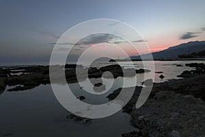 Pink and blue sunset on the beach in Creta, Greece. Beach with blacks rocks and waves at dusk