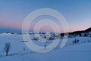 Pink-blue sunset over a snow-covered village on the edge of a forest in a mountain valley