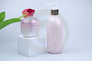 Pink bottle dispenser and pink cosmetic cream jar on a white product display and red tulip on the white background