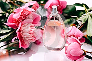 Pink bottle of women`s perfume between peony flowers, close up. Spring gentle fragrance for women.