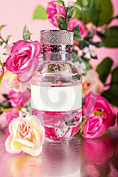 Pink bottle of women`s perfume and peony flowers on a pink background. A gentle spring fragrance for women