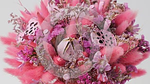 Pink bouquet of different beautiful dried flowers rotates around the axis on a white background