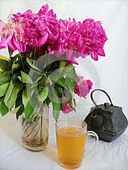 pink bouquet of wilted peony flowers, a cup of green tea and a tea pot