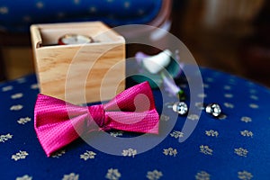 Pink bow tie, beautiful glass cufflinks, flower boutonniere. A men's set of accessories on an old wooden chair with a soft blue s