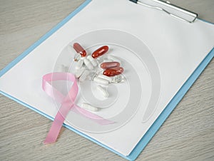 Pink bow and Vitamin capsule or medicine on patient chart  background. medicine for charity cancer treatment, healthcare concept