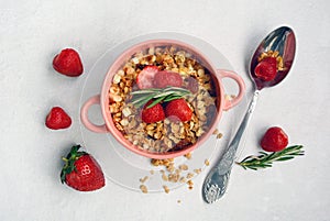 Pink bowl with muesli and strawberries, spoon, rosemary on a light background