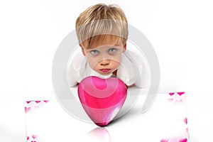 Pink box in a shape of heart with a child boy with a facial attitude ready to kiss someone