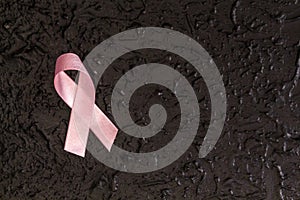 Pink breast cancer awareness ribbon on a dark, black background