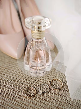 Pink bridal accessories. Golden wedding rings and engagement ring with a diamond, perfume bottle and dust pink, powdery shoes