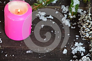 Pink burning candle with christmas decoration, fir tree, baubles and ribbon, in front of a white wooden wall or