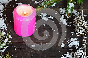 Pink burning candle with christmas decoration, fir tree, baubles and ribbon, in front of a white wooden wall or