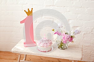 Pink cake with number one and pink wooden number one with golden crown