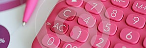 Pink calculator lying on documents with graphs near ballpoint pen closeup