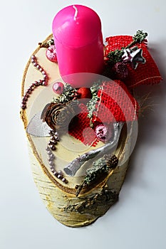 Pink candle on Christmas decorated wooden stand with shiny beads, silver painted wood piece, red fabric knot and cones